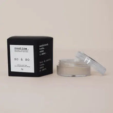 Load image into Gallery viewer, A skincare product shown with its black square box and an open clear jar containing a light beige cream, set against a solid warm beige background. The brand name 'routine.