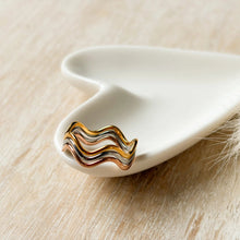 Load image into Gallery viewer, A gold wavy ring with layered silver and rose gold details, displayed on a white ceramic dish over a light wood surface.