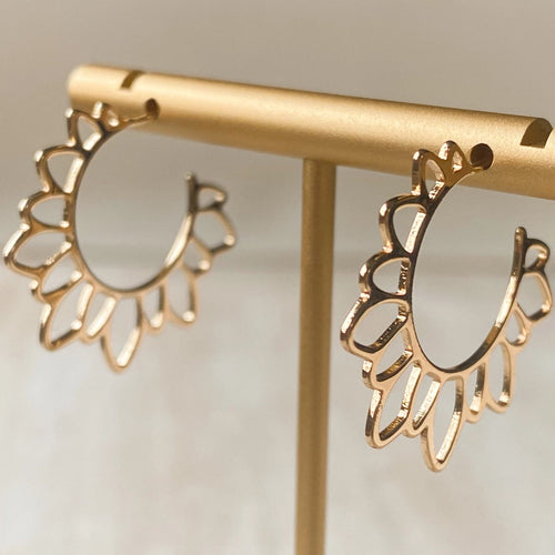 Gold hoop earrings on a gold stand against a neutral background