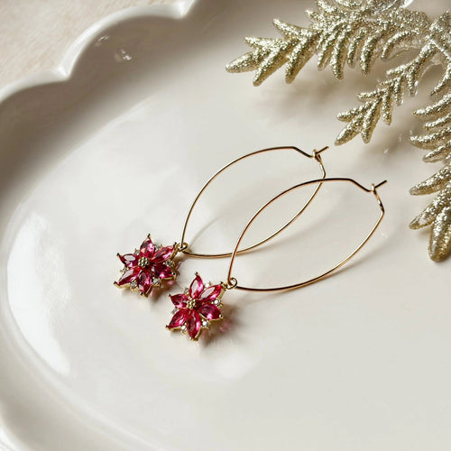 Gold hoop earrings with pink floral charms on a white plate with decorative leaves.