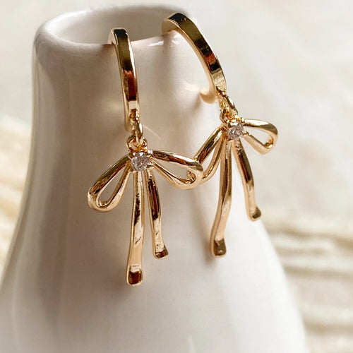 Gold hoop earrings with bow design on a white stand