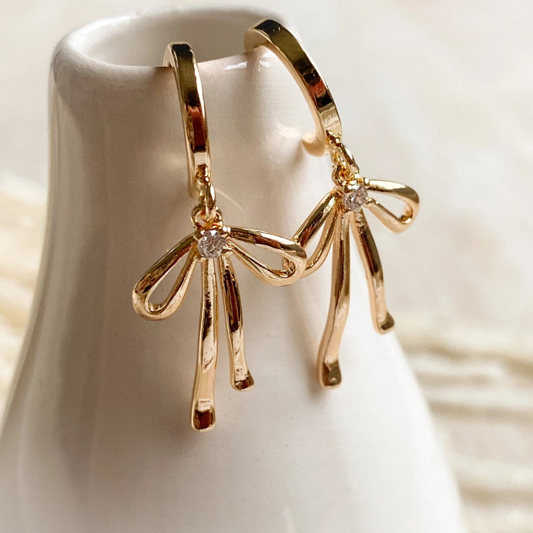 Gold hoop earrings with bow design on a white stand