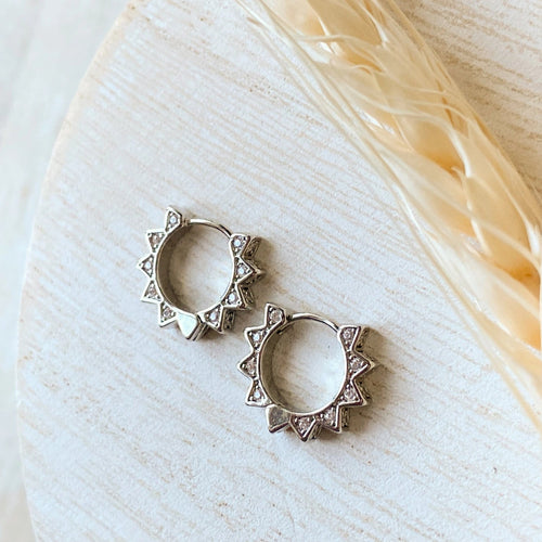 Silver hoop earrings on a light background with feathers