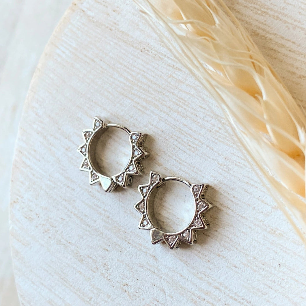 Silver hoop earrings on a light background with feathers