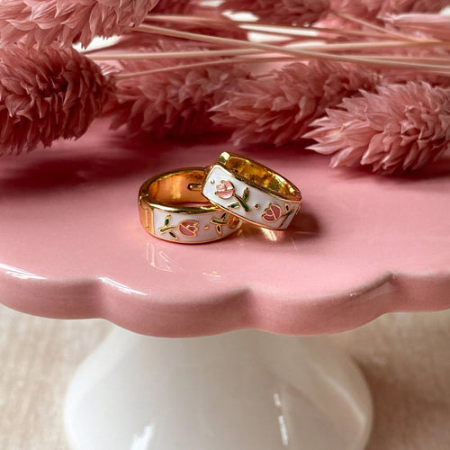 earrings with floral design on a pink stand with pink flowers in the background